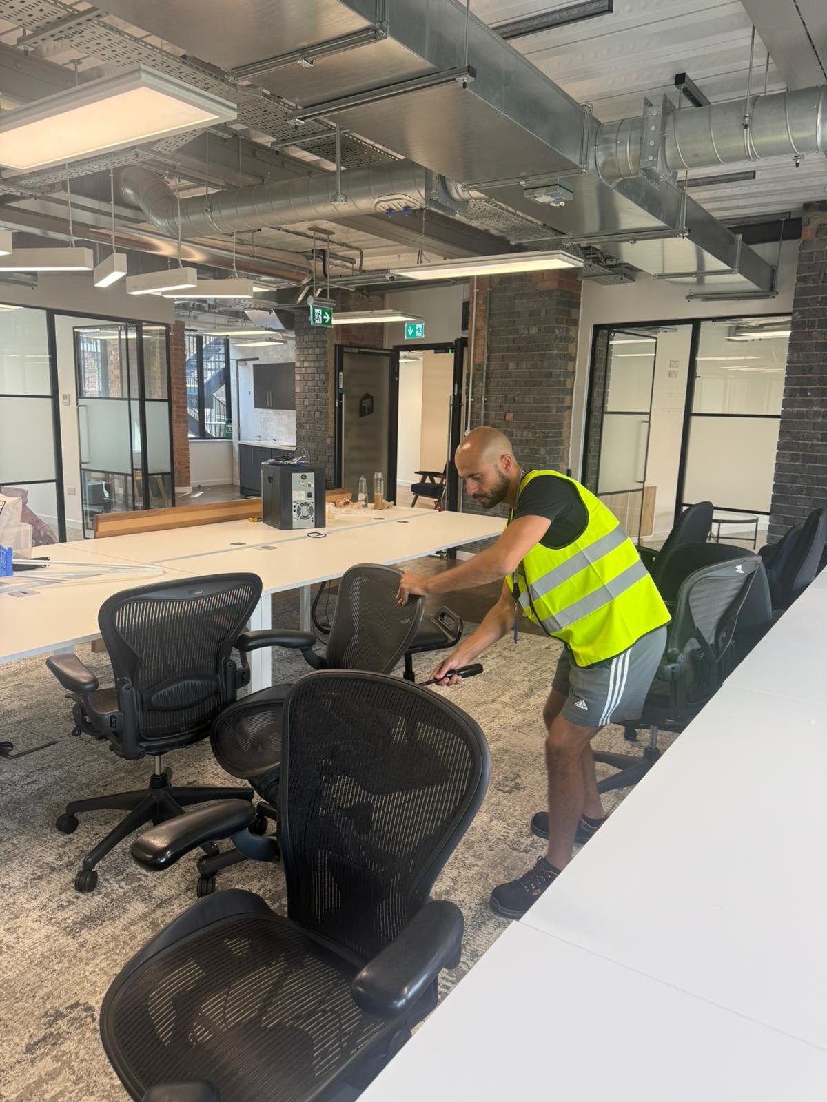 OfficeMatrix team member in a hi-vis vest arranging ergonomic mesh office chairs across an office floor